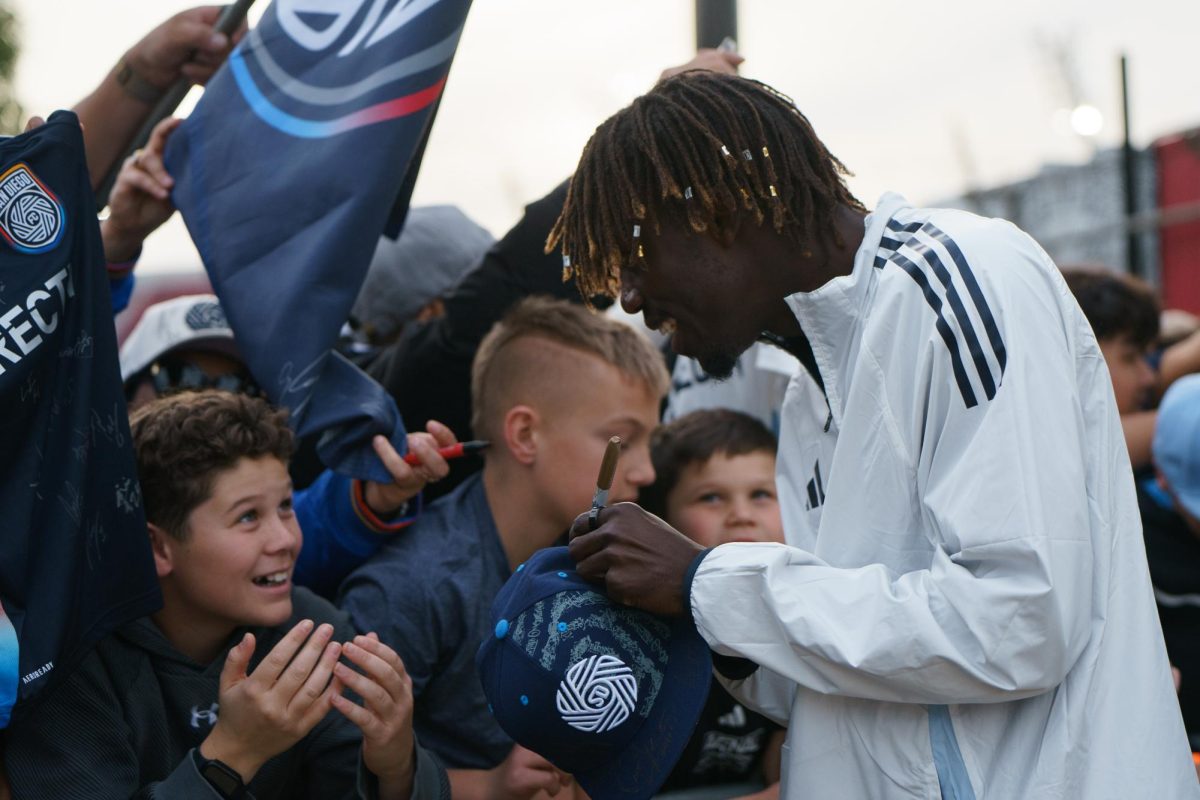 Manu Duah laughs with a young fan as he signs his hat at the San Diego FC kickoff party at Snapdragon Stadium on Feb. 16. 